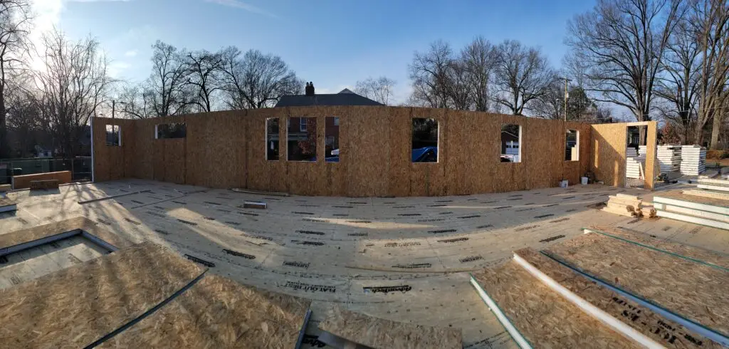 Wide view of SIP walls framed for a Charlotte, NC home, showing the full footprint with window openings and roof trusses stacked nearby