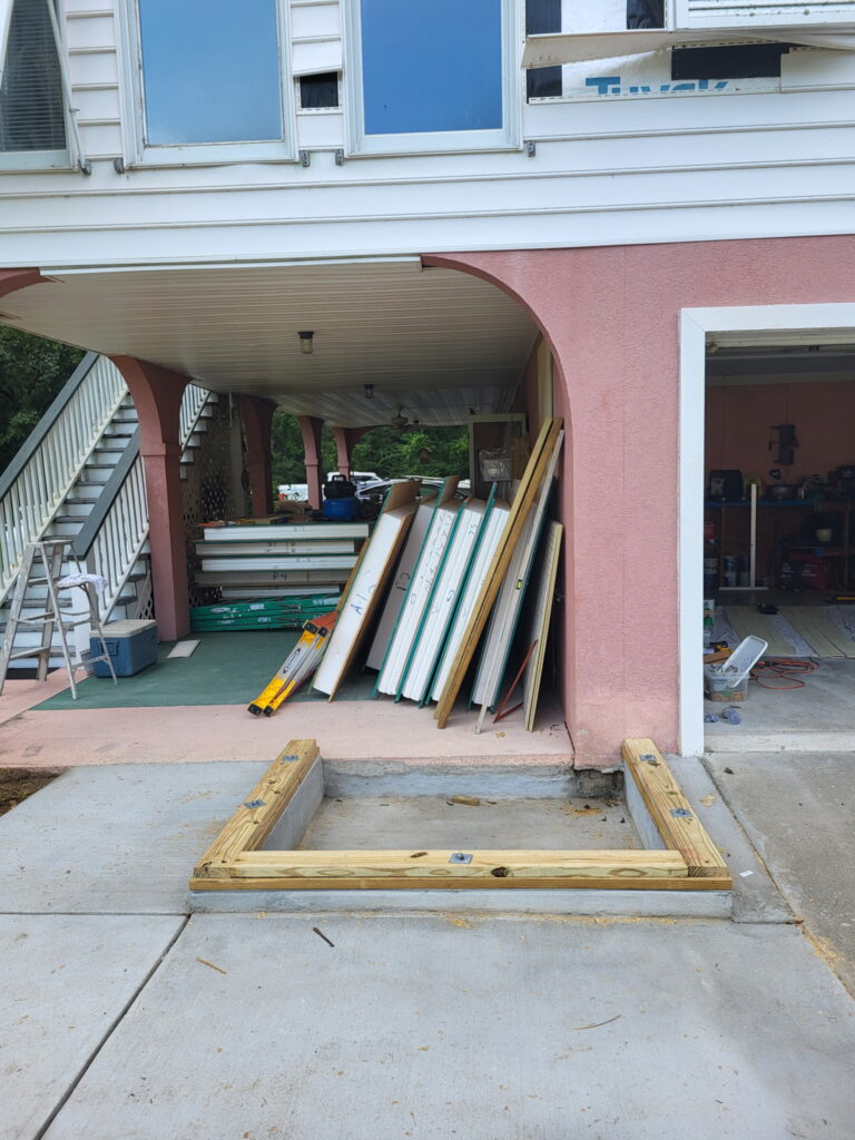New concrete pad and pressure-treated sill framing for the SIP elevator shaft foundation at the garage entrance of the Meggett, South Carolina home, with stacks of SIP panel stock staged against the wall.