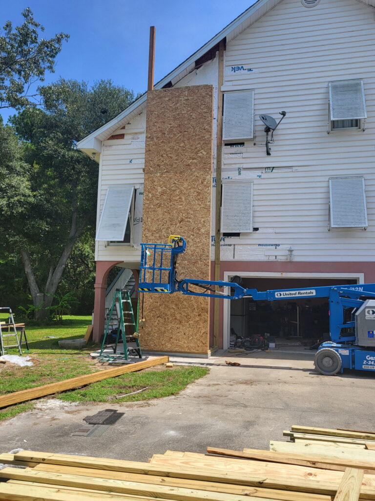 Close-up of the SIP elevator shaft's gable end on the Meggett, South Carolina home, with OSB sheathing newly installed over the wall panels next to the existing vinyl siding and window AC units.