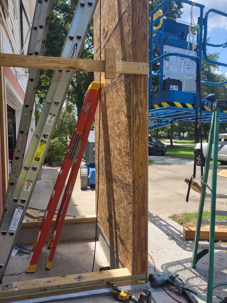 Close-up of an engineered wood column connection on the SIP elevator shaft, with OSB panel sheathing, a ladder and the boom lift visible in the background at the Meggett, South Carolina job site.